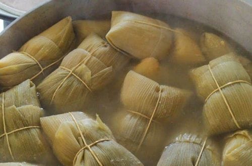 Humitas amarradas cocinándose en una olla grande con agua hirviendo.
