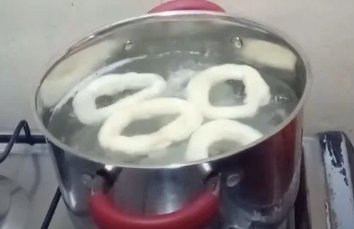 Hervido de las roscas Rosquillas de masa flotando en una olla de agua hirviendo.