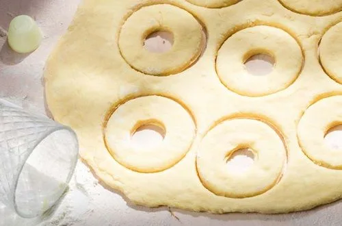 Donas caseras Donas cortadas en su forma de anillo, listas en una bandeja para el segundo levado y la cocción.