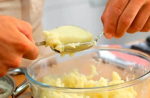 Uso de dos cucharas (técnica quenelle) para formar y verter las porciones de masa de suspiros de monja en el aceite caliente.