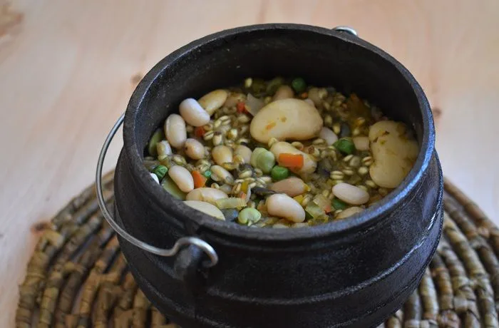 Receta de pisku mapuche Olla de hierro con pisku mapuche, un guiso de porotos, mote, habas y verduras, servido con cilantro fresco.