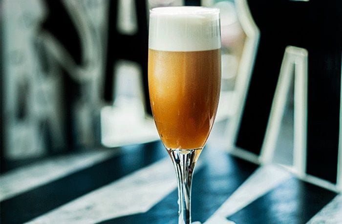 Copa de bitter batido chileno servido en copa flauta con espuma densa en la superficie y una rodaja de limón.