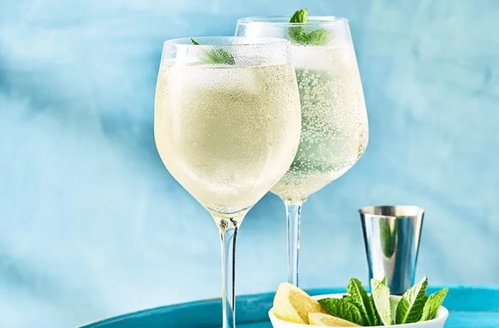Receta de cóctel yugoslavo Cóctel yugoslavo servido en una copa alta con una mezcla dorada de cerveza y vino blanco, decorado con una rodaja de limón.