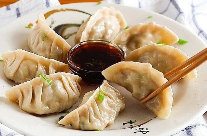 Un plato con gyozas japonesas doradas por la base y tiernas por arriba, dispuestas en círculo alrededor de un pequeño pocillo con salsa de soya y sésamo.